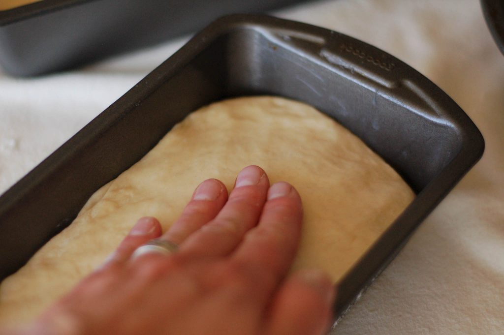 hand preparing bread dough in bread tin