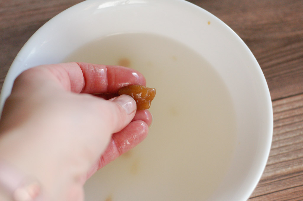 a hand holding some caramel in cold ice water to test for soft ball stage