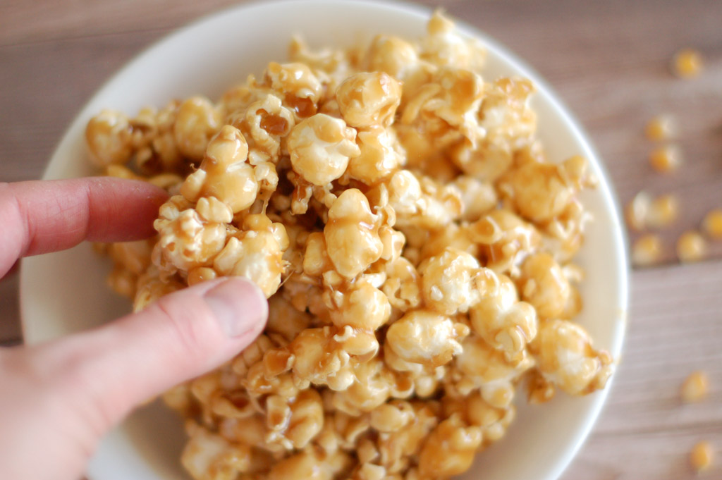 a hand reaching into a white bowl to grab some gooey caramel popcorn