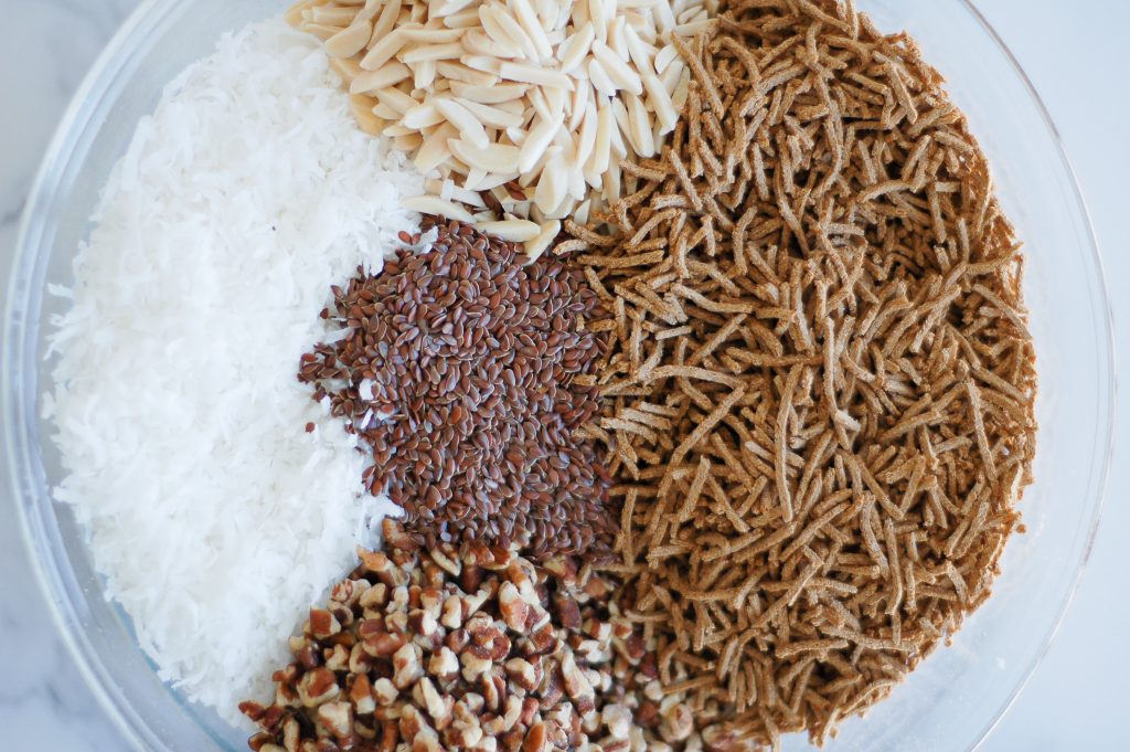 large bowl filled with old fashioned oats, coconut, chopped pecans, bran, sliced almonds, and flax seeds