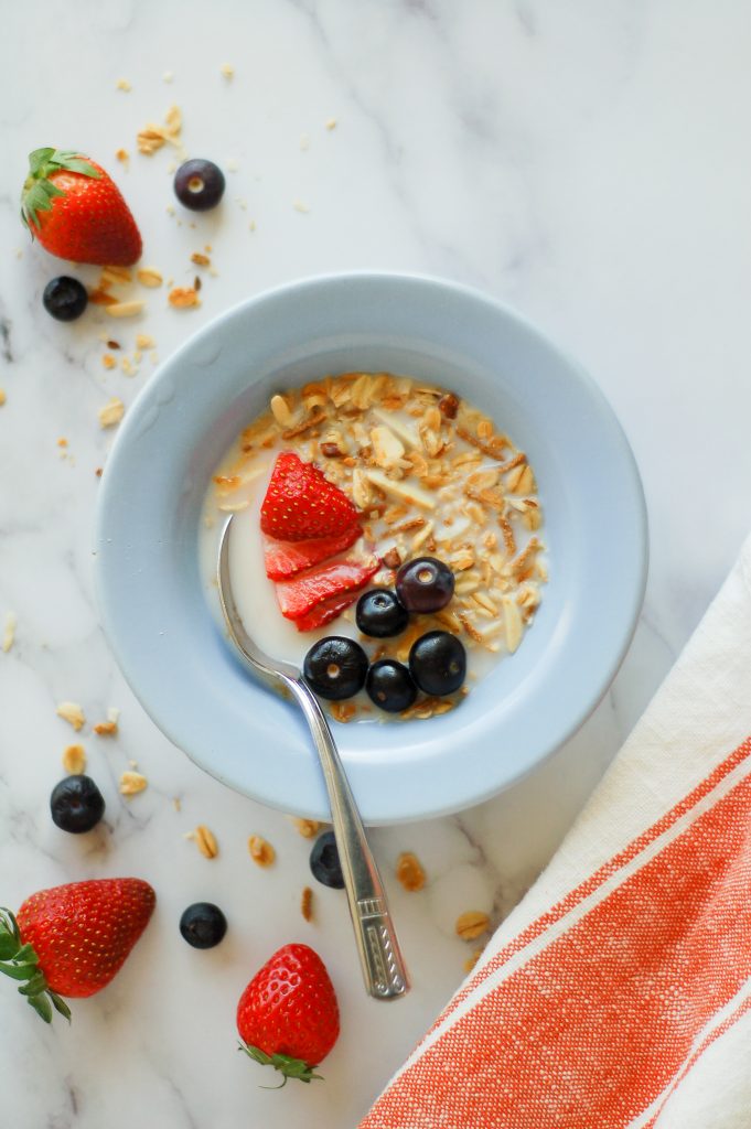 bowl with homemade granola and fresh strawberries and fresh blueberries with almond milk