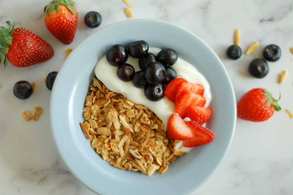 blue bowl filled with homemade granola, vanilla yogurt, and fresh berries