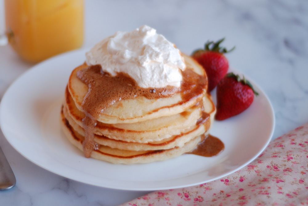 four fluffy homemade pancakes topped with syrup and whipped cream 
