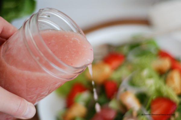 Homemade vinaigrette pouring out of a glass jar onto a green salad